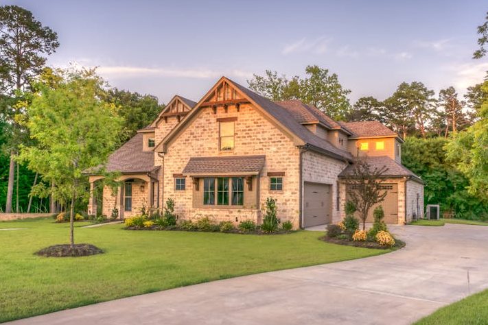 Elegant stone family home surrounded by trees, lush lawn, and vibrant garden.